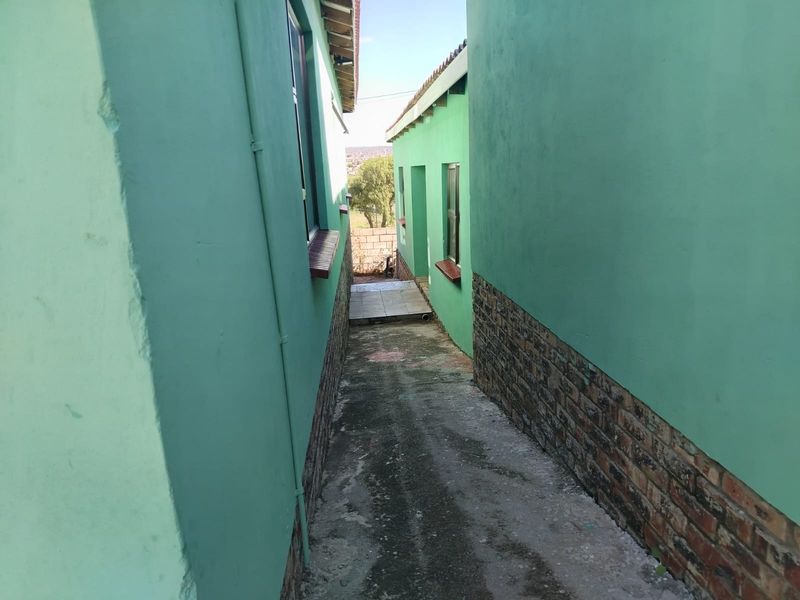 A narrow exterior side passage between two building sections featuring painted walls with brick cladding and a concrete walkway.