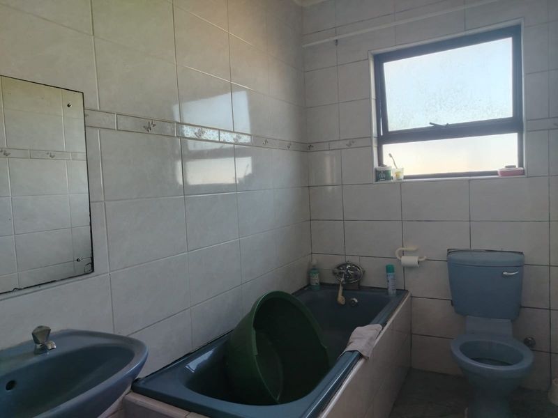 A dated bathroom featuring blue sanitaryware, including a bathtub, toilet, and washbasin, with neutral wall tiling and a window for natural light.