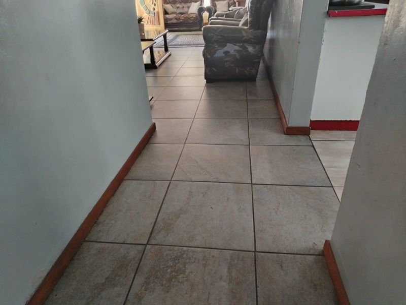 A tiled hallway connecting living spaces, featuring neutral ceramic flooring and wooden skirting boards.