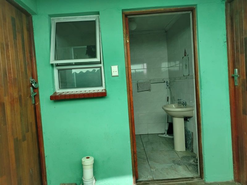 A small bathroom featuring a pedestal basin, tiled walls and flooring, and a top-hung window, requiring cosmetic updates to improve its overall condition.