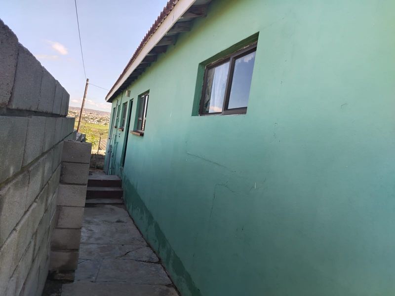 Side exterior view of the property showing a concrete pathway, boundary wall, and painted exterior walls with visible signs of wear and cracking.