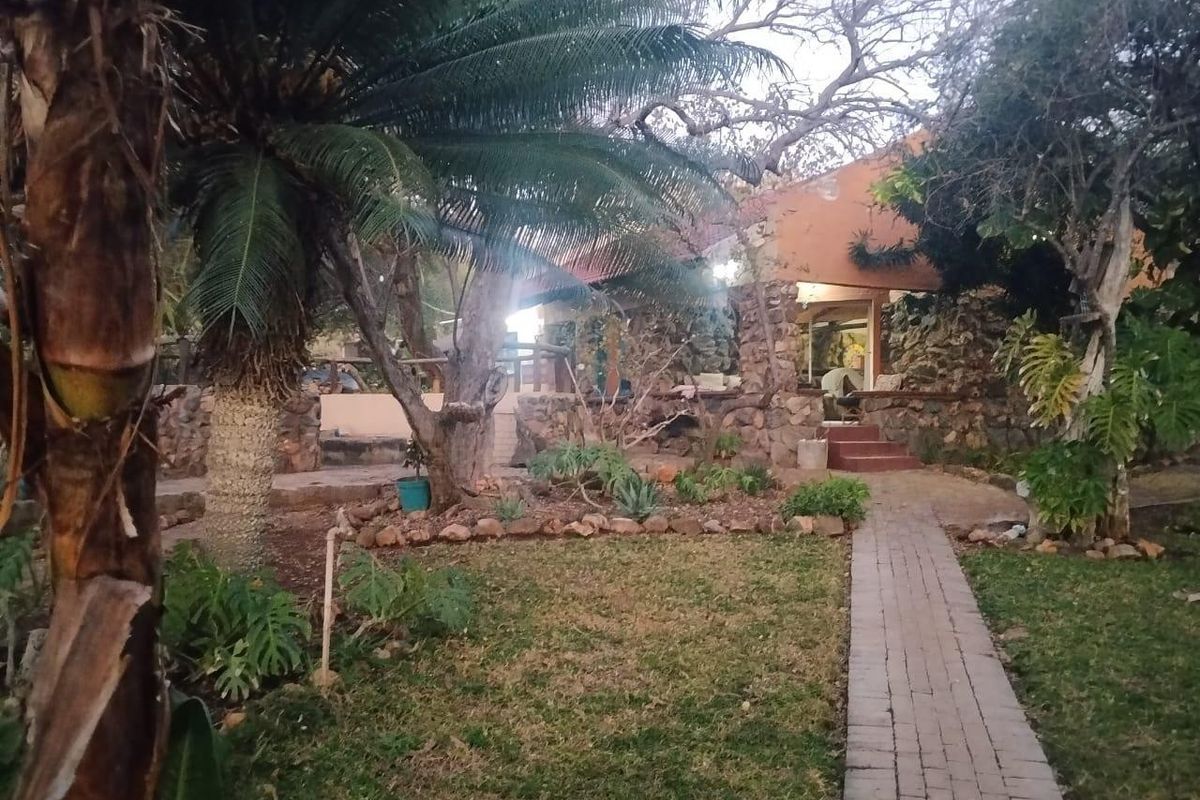 A rustic rear garden area featuring stone-clad walls, a brick paved pathway, and a covered patio space set within a mature landscaped environment.