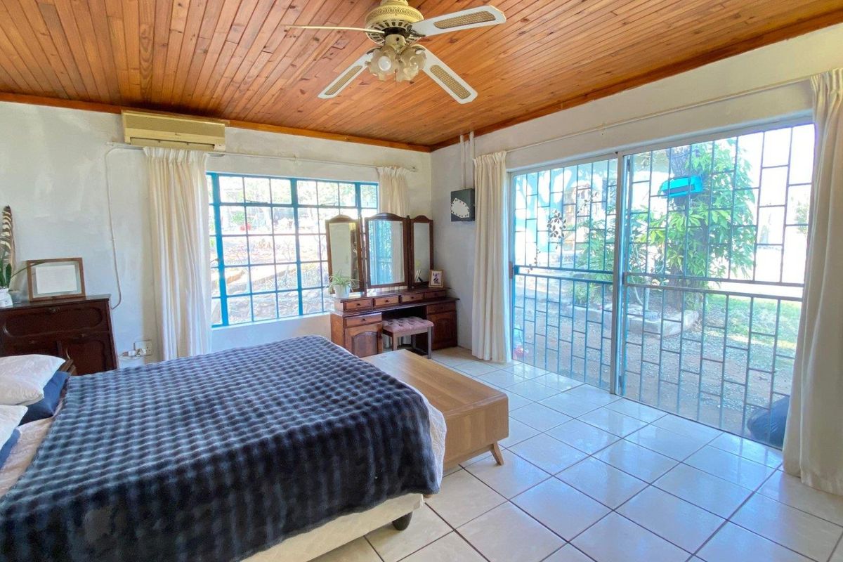 Spacious bedroom featuring a timber ceiling, ceiling fan, split-system air conditioning, tiled floors, and sliding glass doors with security bars leading to the exterior.