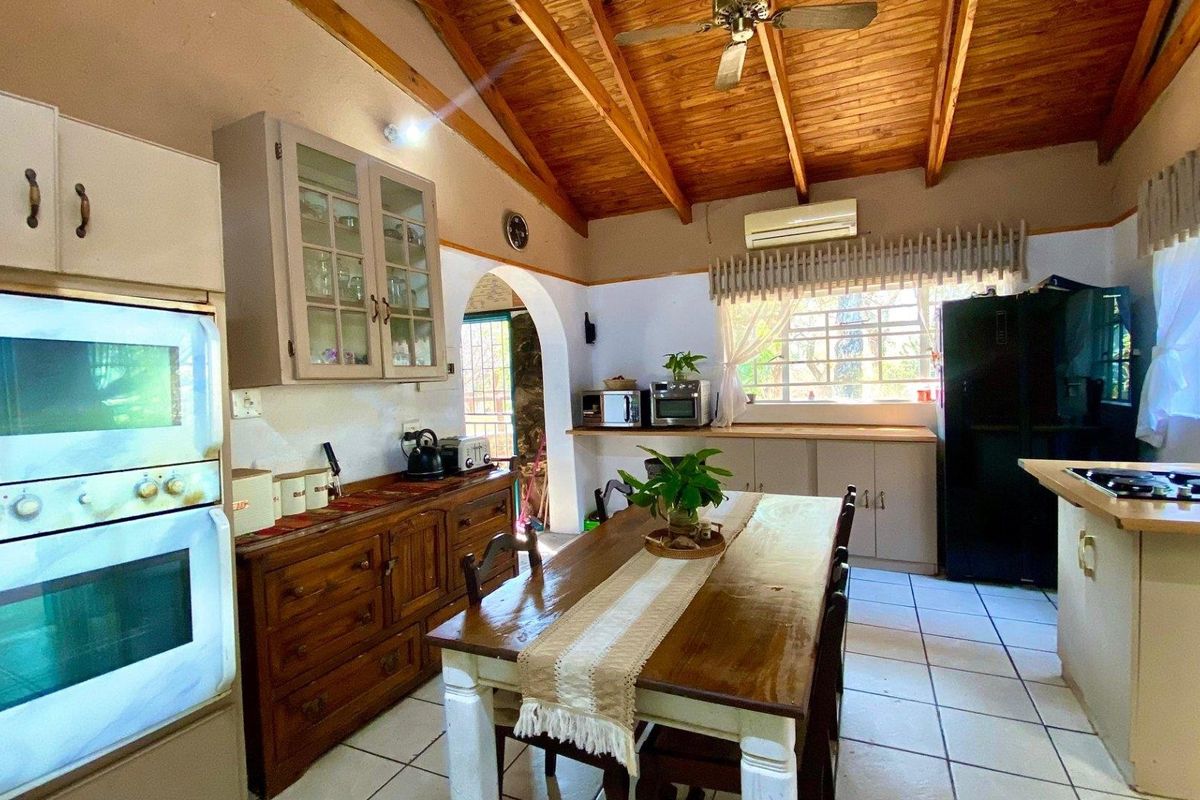 Spacious farmhouse kitchen featuring exposed timber ceilings, tiled flooring, built-in cabinetry, and integrated cooking appliances with a dining area.