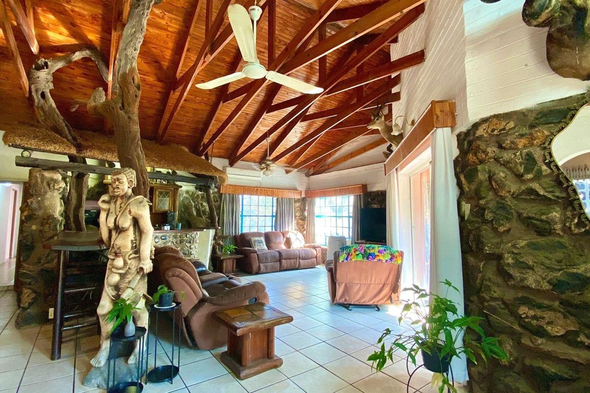 Spacious living room featuring a vaulted timber ceiling with exposed rafters, stone feature walls, tiled flooring, and direct access to the outdoors.