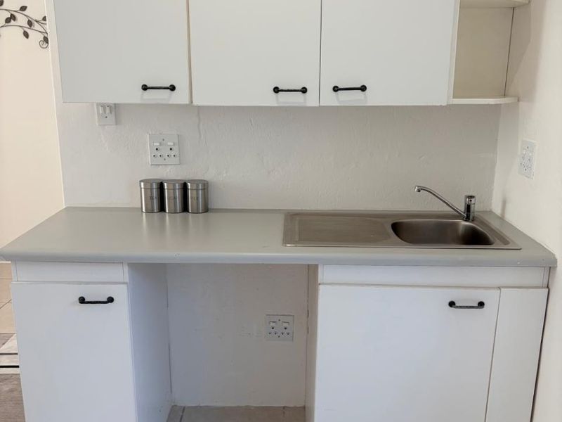 A functional scullery or utility area featuring white built-in cabinetry, a stainless steel sink, and tiled flooring.