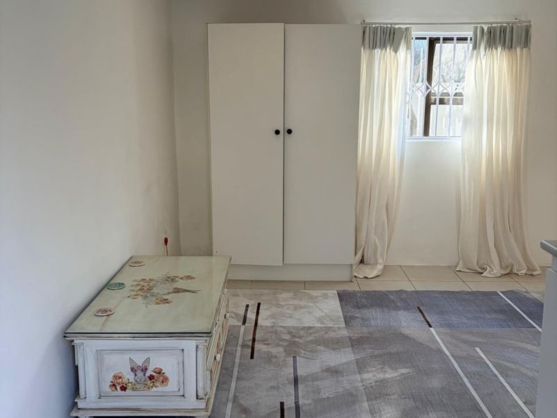 A bedroom featuring tiled flooring, a built-in wardrobe, and a window fitted with security bars, offering a clean and functional living space.