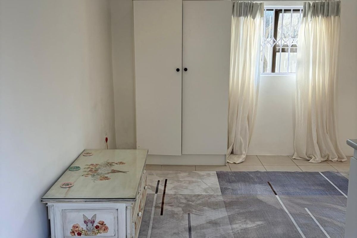 A bedroom featuring tiled flooring, a built-in wardrobe, and a window fitted with security bars, offering a clean and functional living space.
