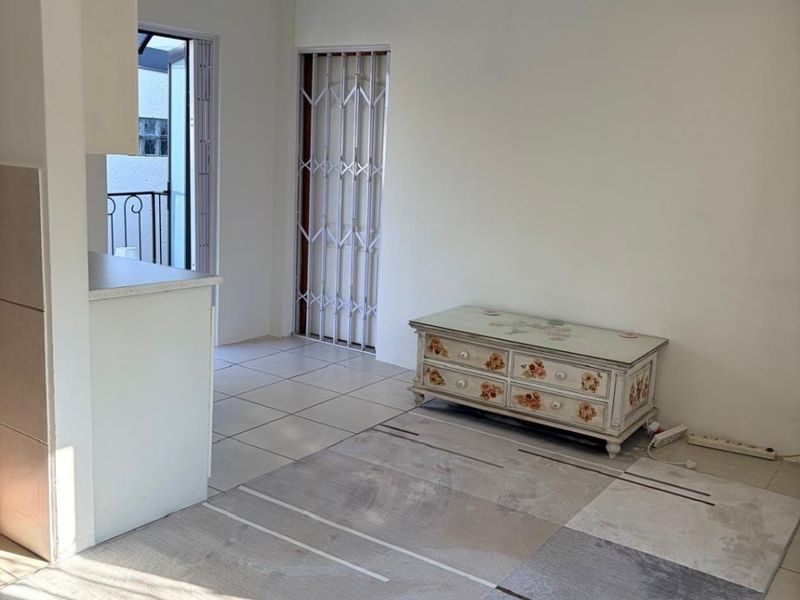Open plan living area featuring tiled flooring, recessed downlights, and direct access to a balcony through a security gate.