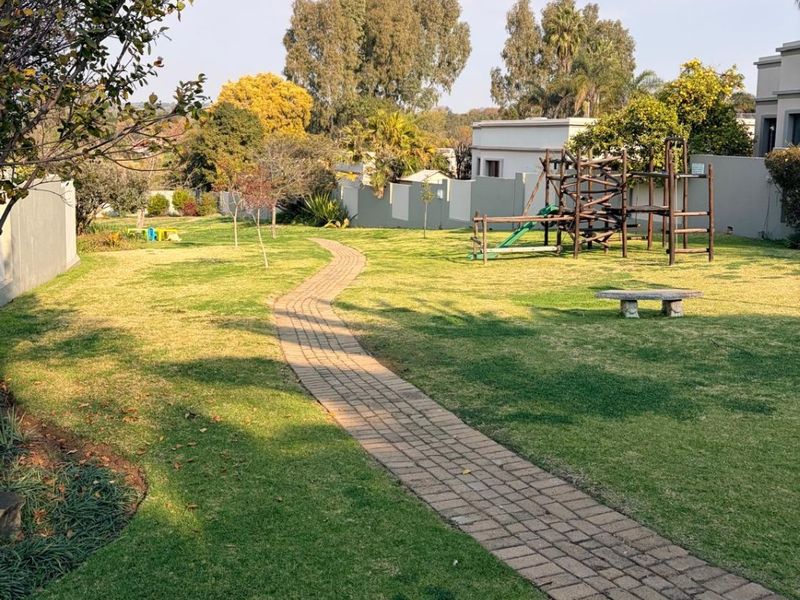 A well-maintained garden featuring a winding paved walkway, expansive lawn, and perimeter boundary walls.