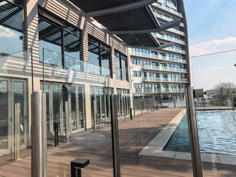 Modern apartment complex pool area featuring a swimming pool, timber decking, glass balustrades, and a louvre pergola structure.