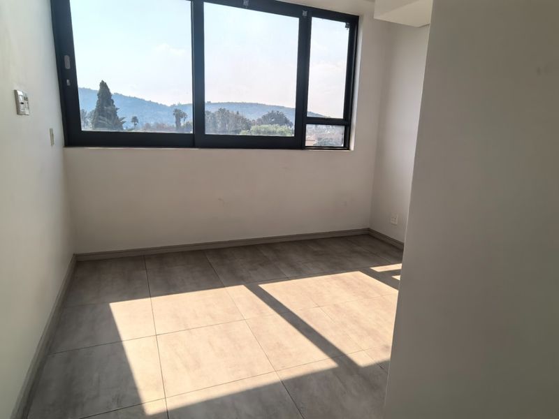 A bright, empty bedroom featuring large windows with scenic views and neutral tiled flooring, offering a clean canvas for personalization.