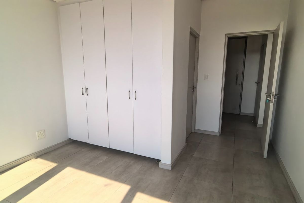 A bright, empty bedroom featuring neutral tiled flooring and ample built-in cupboard storage, offering a clean and versatile space.