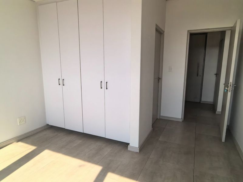 A bright, empty bedroom featuring neutral tiled flooring and ample built-in cupboard storage, offering a clean and versatile space.