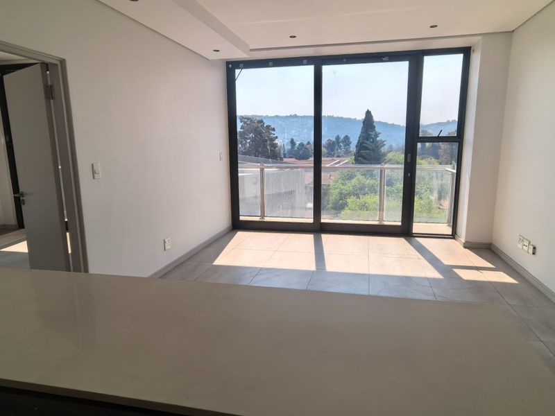 An open-plan living area featuring modern tiled floors, recessed lighting, and large sliding glass doors that open to a balcony with scenic views.