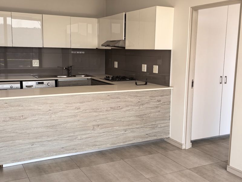 Modern kitchen featuring sleek white cabinetry, wood-look breakfast bar, stone countertops, gas hob, and integrated appliances, finished with neutral floor tiles.