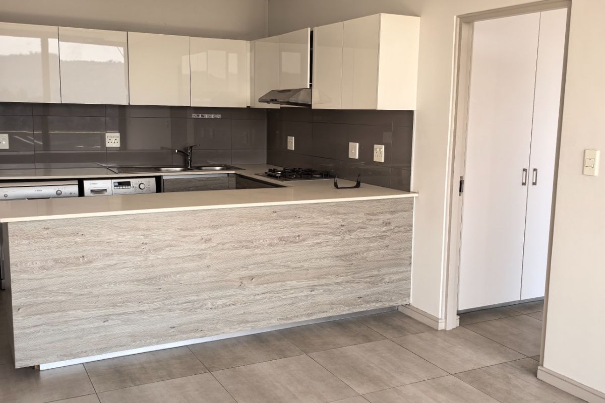 Modern kitchen featuring sleek white cabinetry, wood-look breakfast bar, stone countertops, gas hob, and integrated appliances, finished with neutral floor tiles.