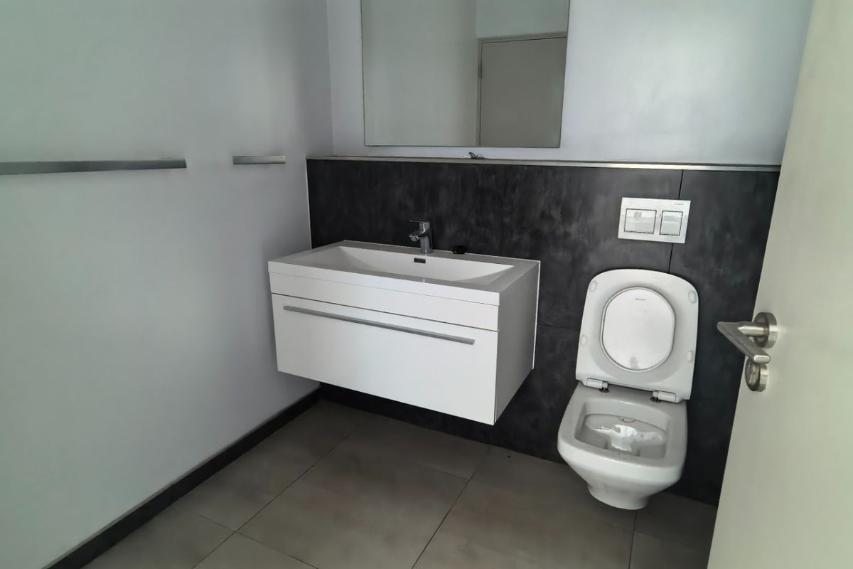 A modern, clean bathroom featuring a wall-mounted vanity, basin, and wall-hung toilet with contemporary dark tiled splashback and neutral floor tiles.