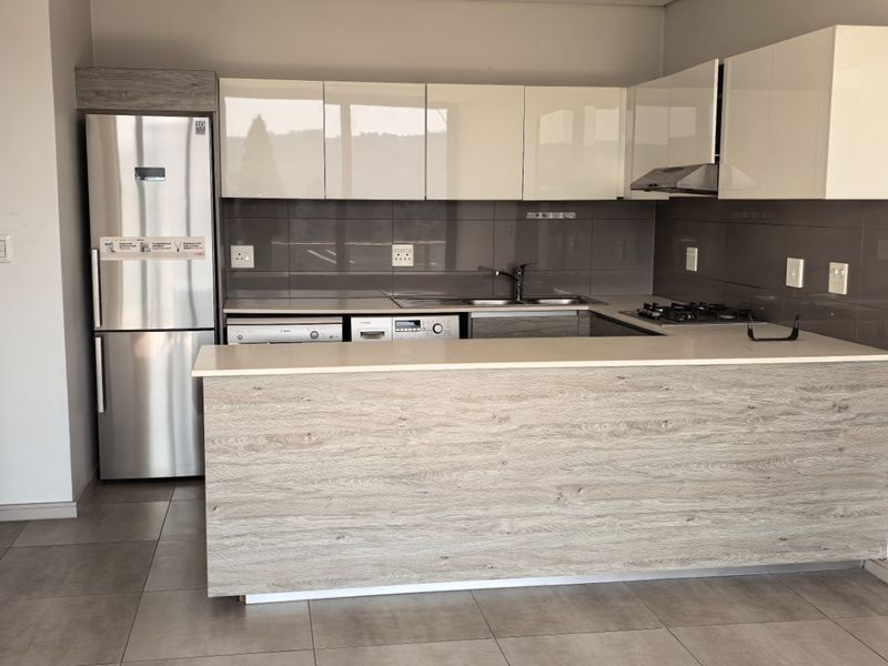 Modern kitchen featuring sleek white cabinetry, stone countertops, a gas hob, extractor fan, and tiled flooring in an open-plan layout.