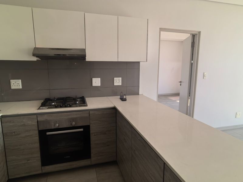 Modern kitchen featuring sleek two-tone cabinetry, stone countertops, integrated gas hob, electric oven, and extractor fan, with neutral tiled flooring throughout.