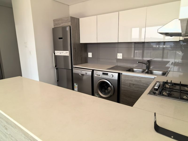 Modern kitchen featuring sleek white and wood-grain cabinetry, stone countertops, a gas hob, extractor fan, and integrated space for appliances.