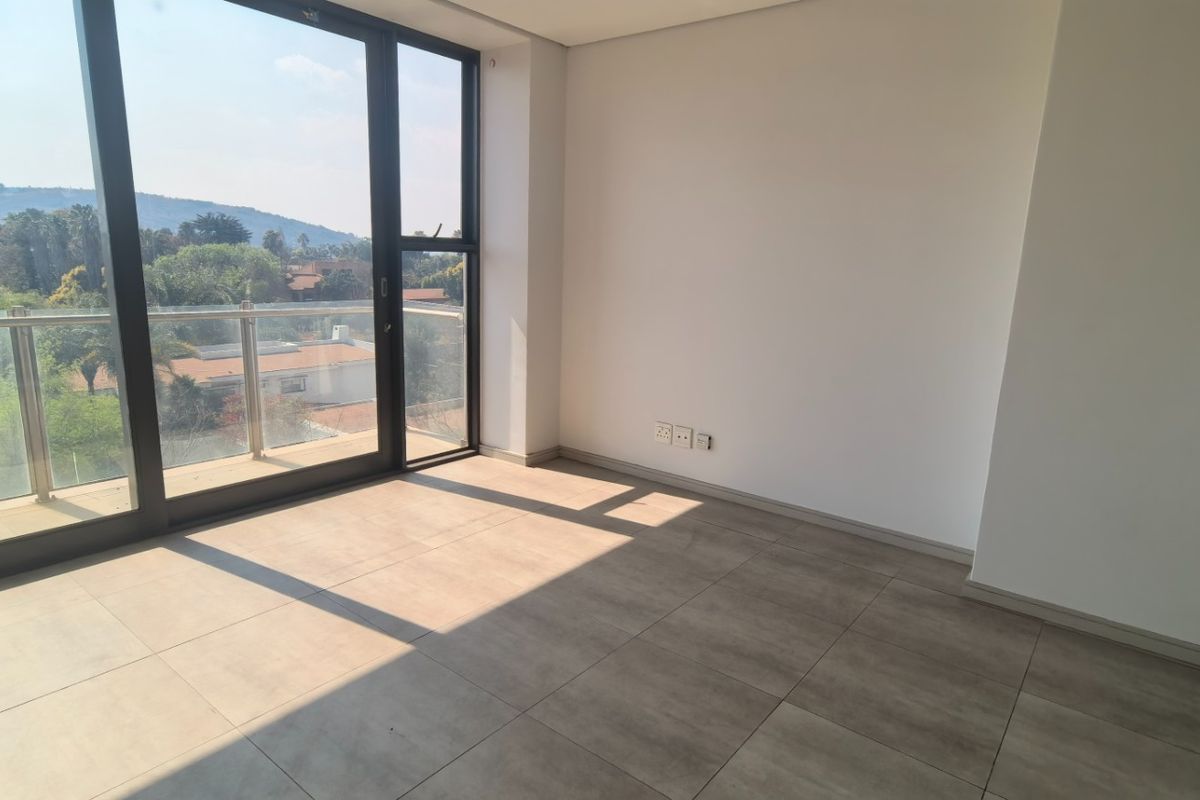 A bright, empty living area featuring large format floor tiles and floor-to-ceiling sliding doors opening onto a balcony with scenic views.