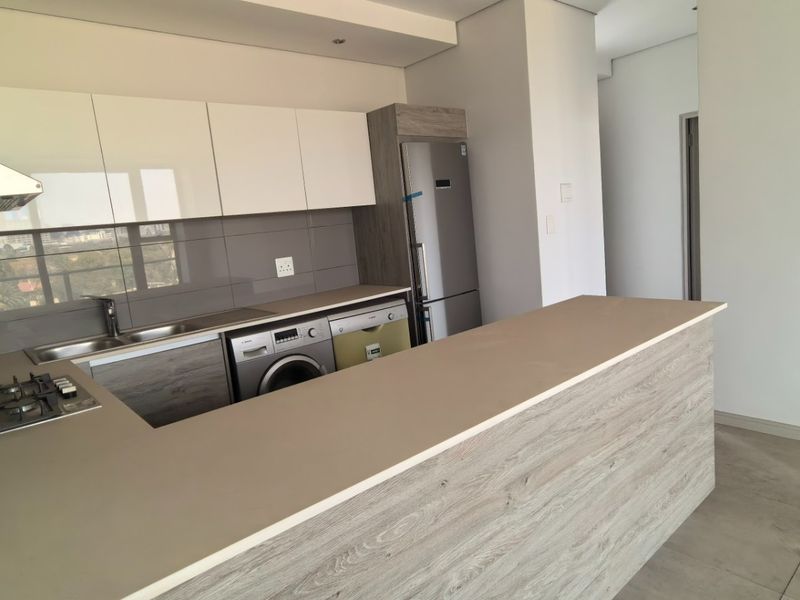 Modern kitchen featuring sleek white and wood-grain cabinetry, stone countertops, a gas hob, and an integrated breakfast bar in an open-plan layout.