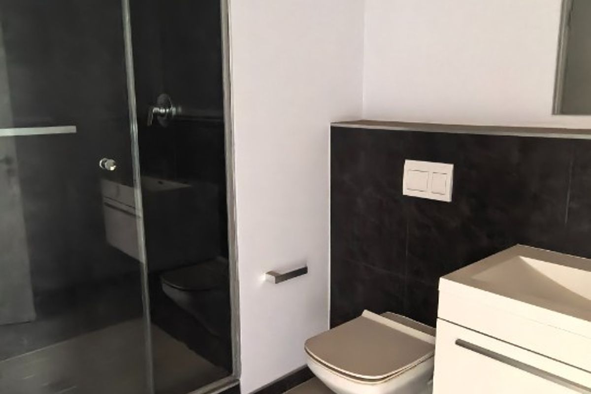 Modern bathroom featuring a glass-enclosed shower, wall-mounted toilet, and a sleek floating vanity with contemporary tiling.