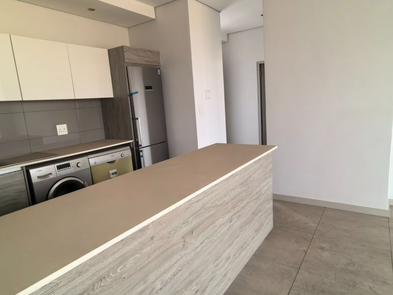 Modern kitchen featuring sleek cabinetry, stone countertops, a breakfast bar, and integrated appliances, finished with neutral porcelain floor tiles.