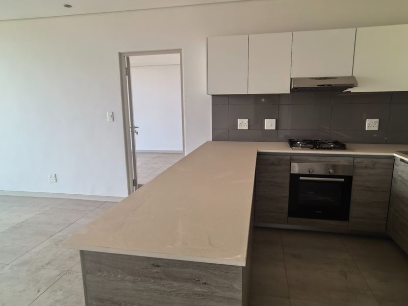 Modern open-plan kitchen featuring sleek cabinetry, integrated appliances, and tiled flooring, seamlessly flowing into an adjacent living area with access to a balcony.
