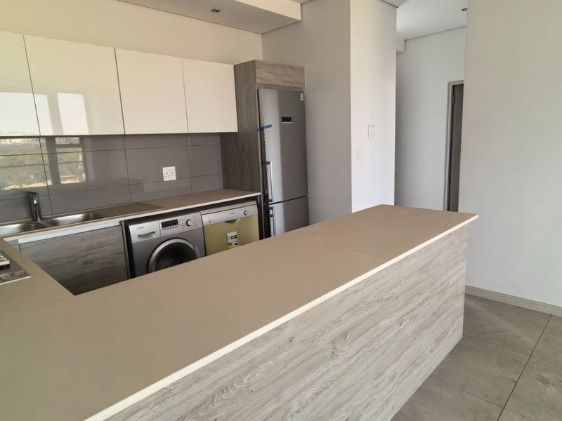 Modern kitchen featuring sleek white and wood-grain cabinetry, stone countertops, a breakfast bar, and integrated gas hob with extractor fan.