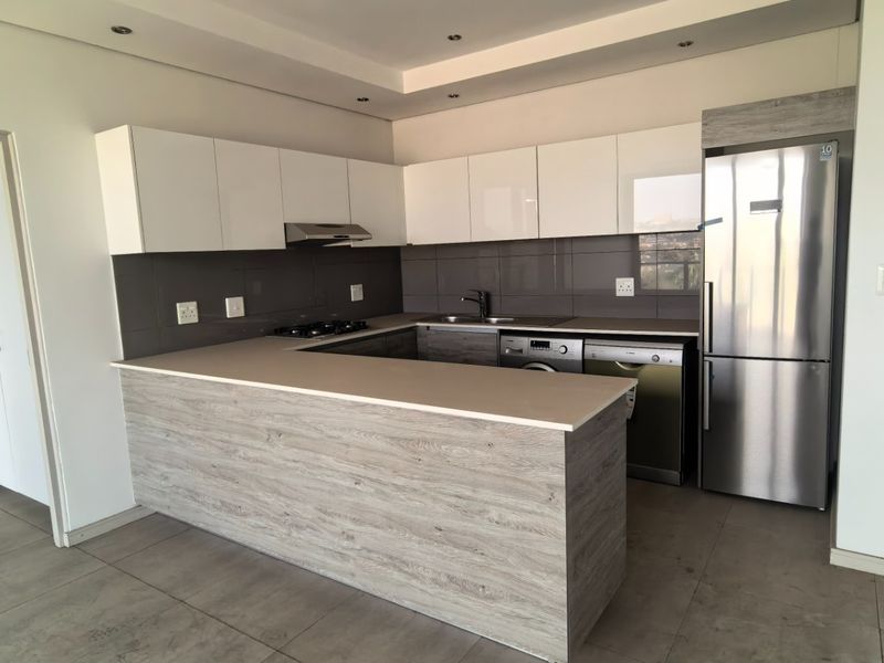 Modern kitchen featuring sleek white cabinetry, wood-grain breakfast bar, stone countertops, and integrated stainless steel appliances in an open-plan layout.