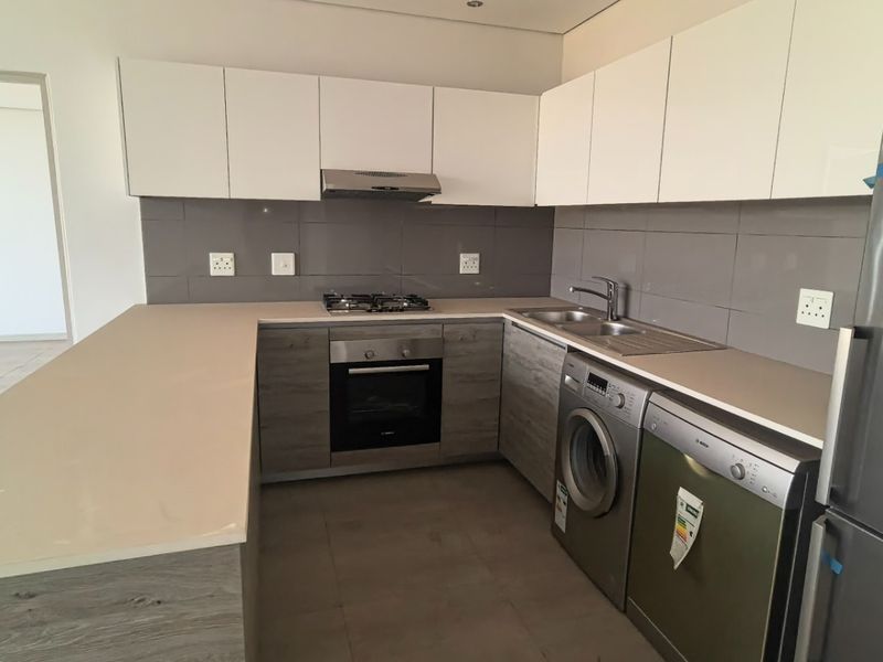 Modern kitchen featuring sleek two-tone cabinetry, stone countertops, integrated gas hob, oven, and extractor fan with a neutral tiled backsplash.