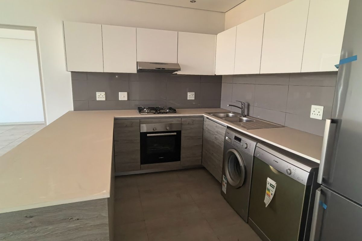 Modern kitchen featuring sleek two-tone cabinetry, stone countertops, integrated gas hob, oven, and extractor fan with a neutral tiled backsplash.