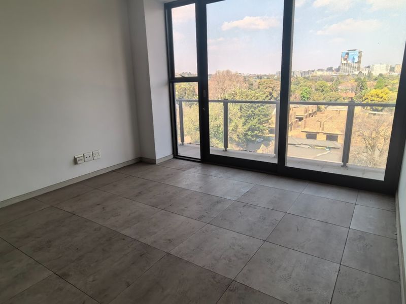 An empty, modern living area featuring large-format floor tiles and floor-to-ceiling glass doors leading to a balcony with an urban view.