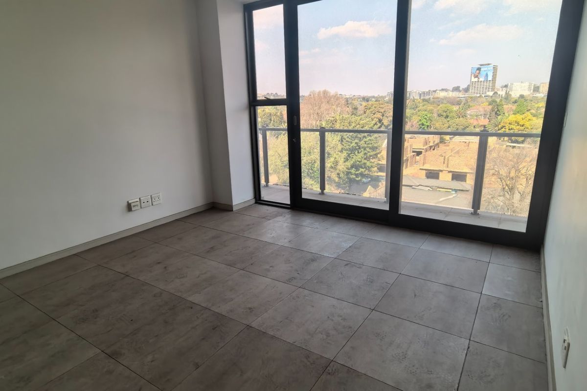 An empty, modern living area featuring large-format floor tiles and floor-to-ceiling glass doors leading to a balcony with an urban view.