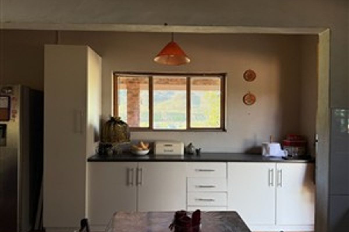 A functional kitchen area featuring built-in cabinetry, dark countertops, and a window overlooking the farm landscape.