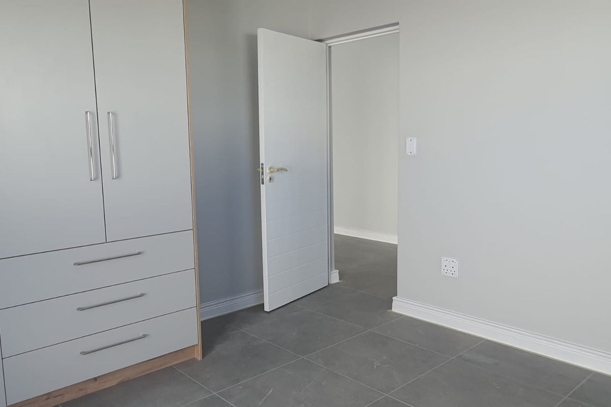 A clean, empty bedroom featuring modern grey floor tiles, neutral walls, and a built-in wardrobe with integrated drawers.