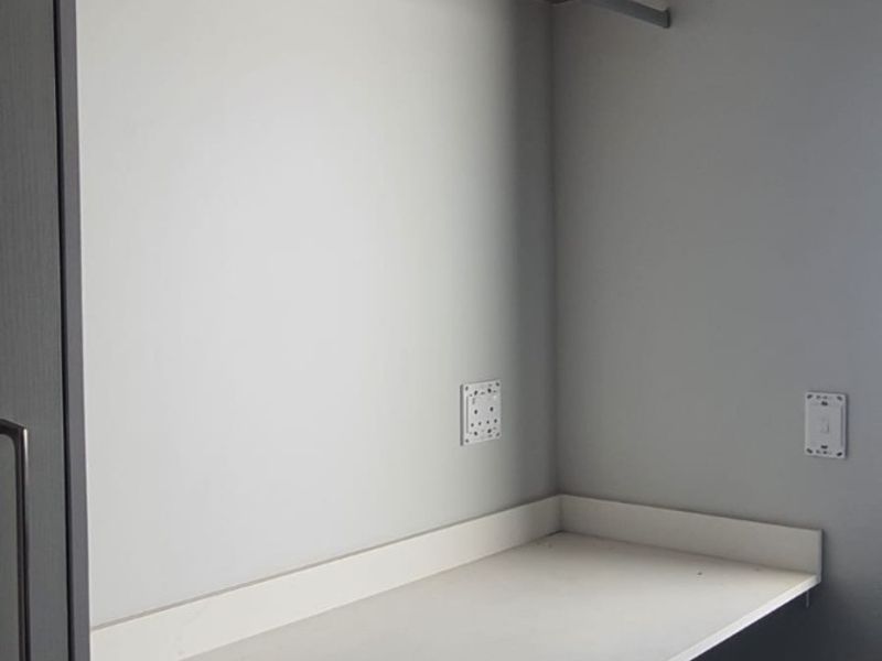 A clean, modern utility space or study nook featuring a built-in desk, floating shelf with hanging rail, and neutral grey finishes.