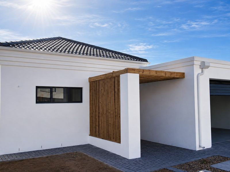 Modern exterior view of the property featuring a clean white facade, tiled roof, timber pergola detail, and a paved driveway leading to the garage.