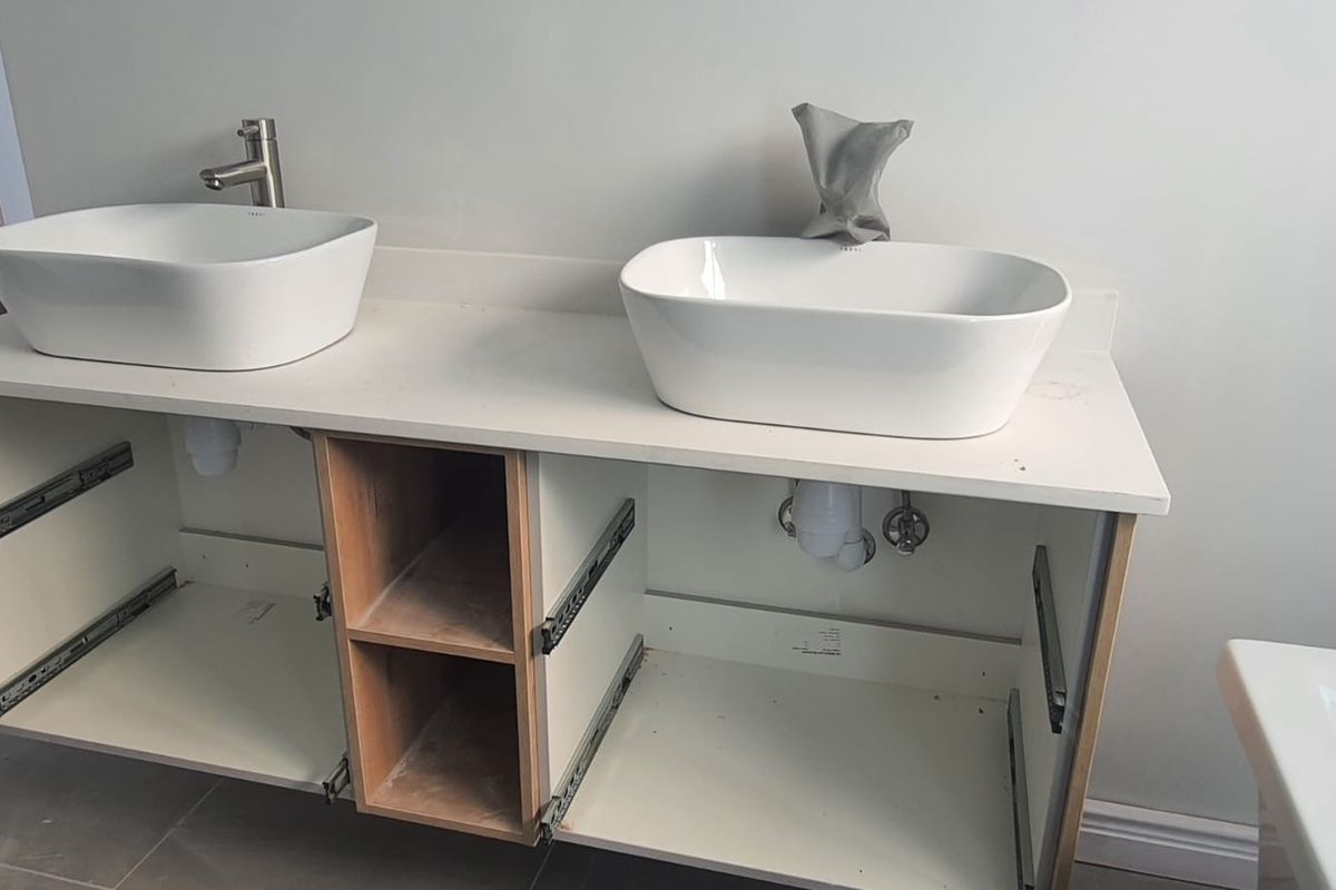 A bathroom vanity featuring dual vessel sinks and a stone countertop, currently missing cabinet doors and drawer fronts, awaiting completion.