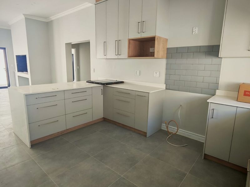 Modern kitchen featuring light grey cabinetry, stone countertops, and subway tile backsplash, currently awaiting final appliance installation and finishing touches.