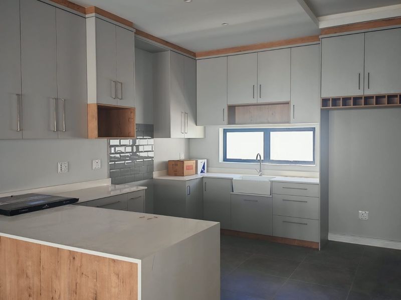 Modern kitchen featuring grey cabinetry with wood accents, quartz countertops, an apron-front sink, and a functional island layout.
