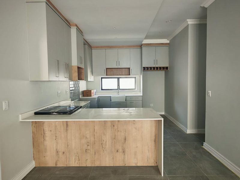 Modern kitchen featuring light grey cabinetry, wood-look island paneling, stone countertops, an apron sink, and sleek tiled flooring in an open-plan layout.