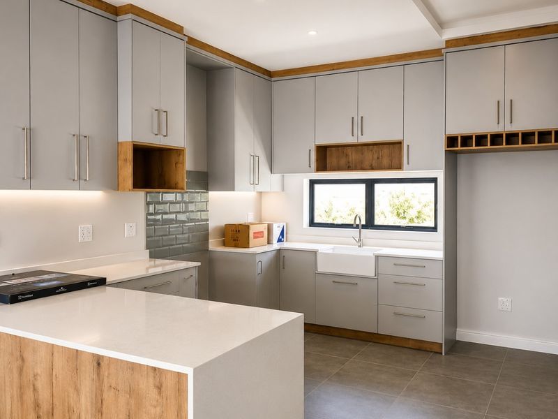 Modern kitchen featuring light grey cabinetry with wood accents, quartz countertops, a farmhouse sink, and a functional island layout.