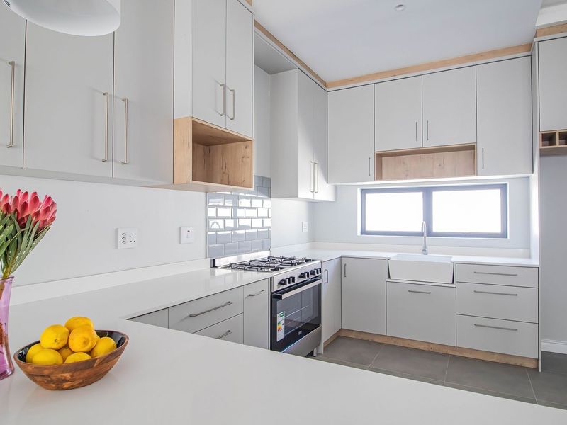 Modern kitchen featuring light grey cabinetry, stone countertops, a gas stove, subway tile backsplash, and a classic apron sink with tiled flooring.