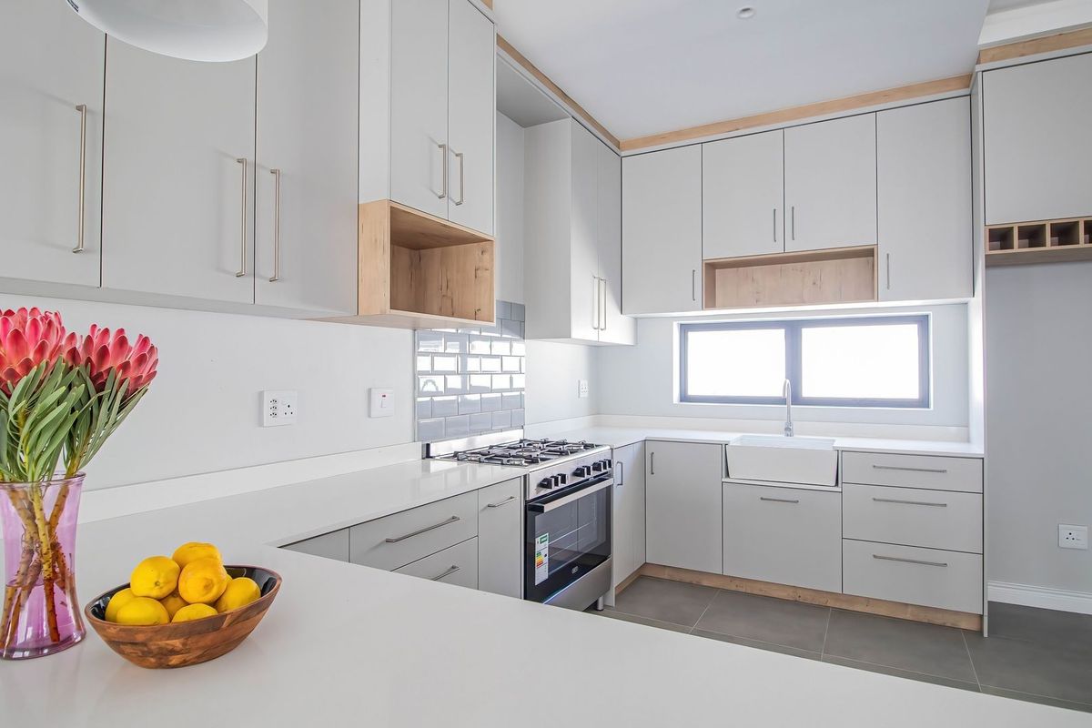 Modern kitchen featuring light grey cabinetry, stone countertops, a gas stove, subway tile backsplash, and a classic apron sink with tiled flooring.