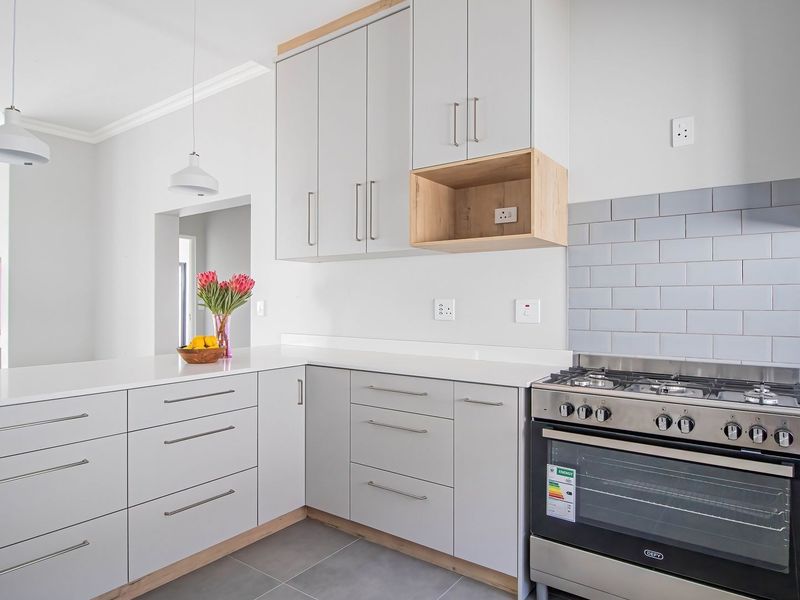 Modern kitchen featuring light grey cabinetry, stone countertops, subway tile backsplash, and a stainless steel gas stove with oven.
