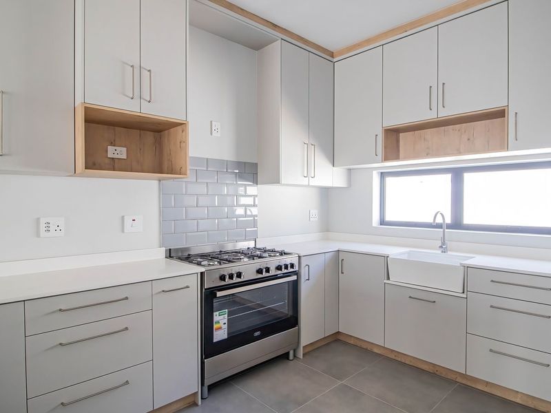 Modern kitchen featuring light grey cabinetry, quartz countertops, a gas stove with oven, subway tile backsplash, and a farmhouse-style apron sink.