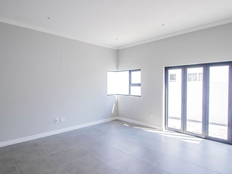 A bright, modern, and empty living area featuring large aluminium stacker doors, neutral tiled flooring, and recessed lighting, offering a clean canvas for interior design.